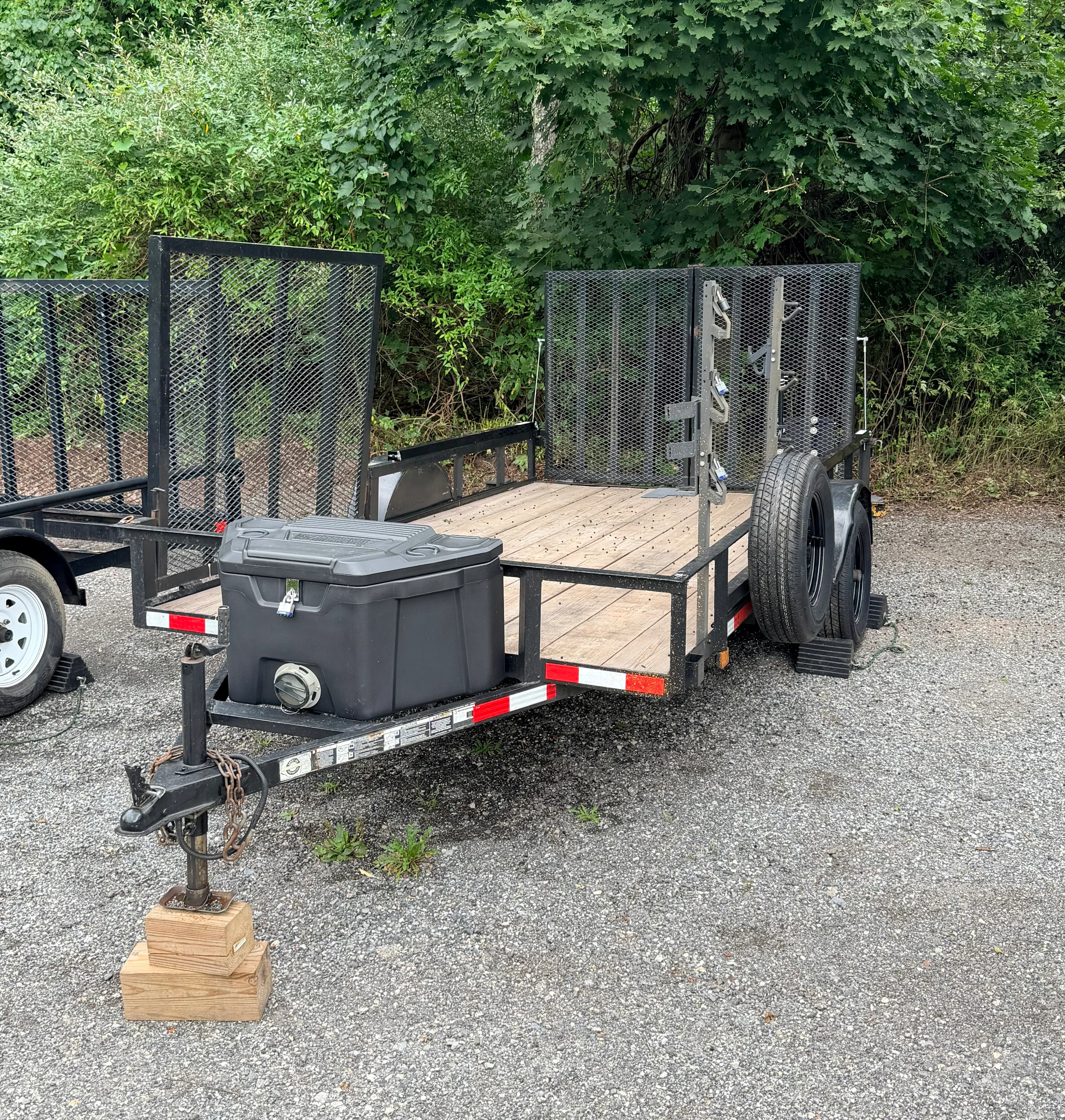Utility trailer with wood deck, black mesh enclosure, storage box, and dual axles