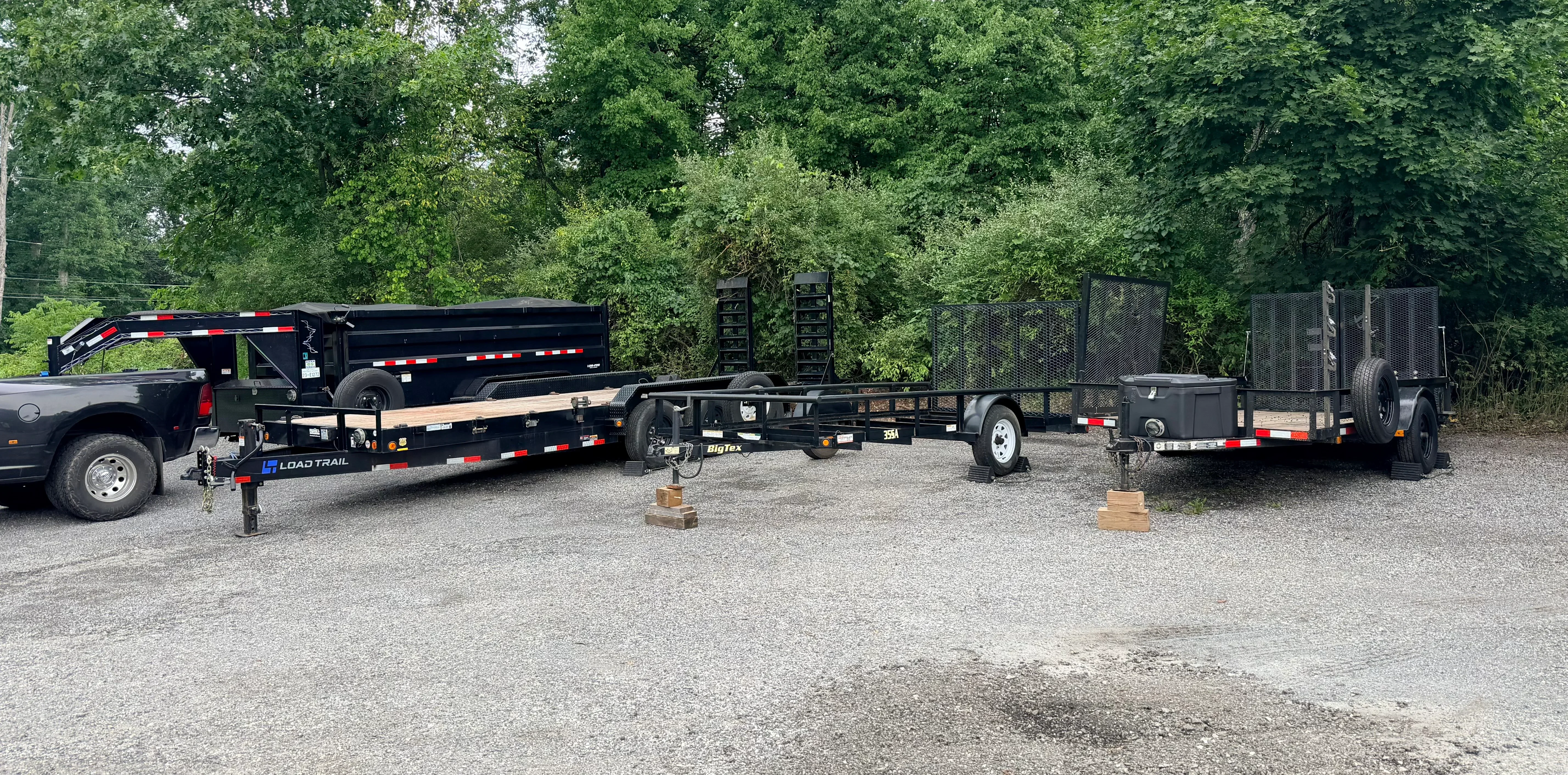 Multiple black utility trailers with red and white striping, flatbed and enclosed designs parked in row